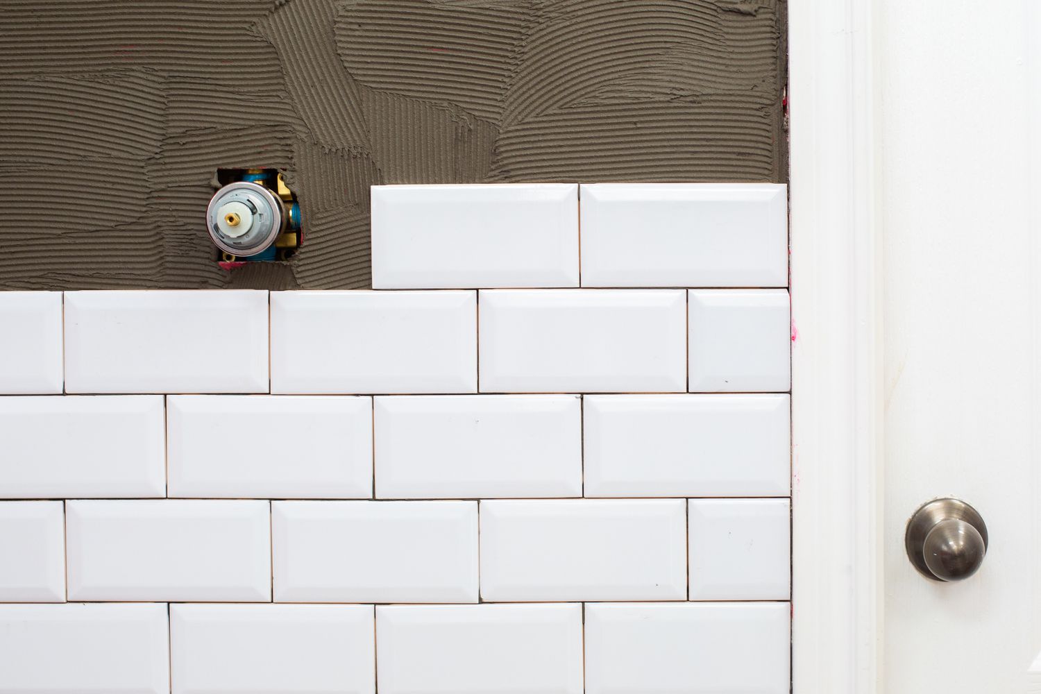 Carrelage mural en céramique blanche installé sur la moitié d'un mur et l'autre moitié exposée avec de l'adhésif