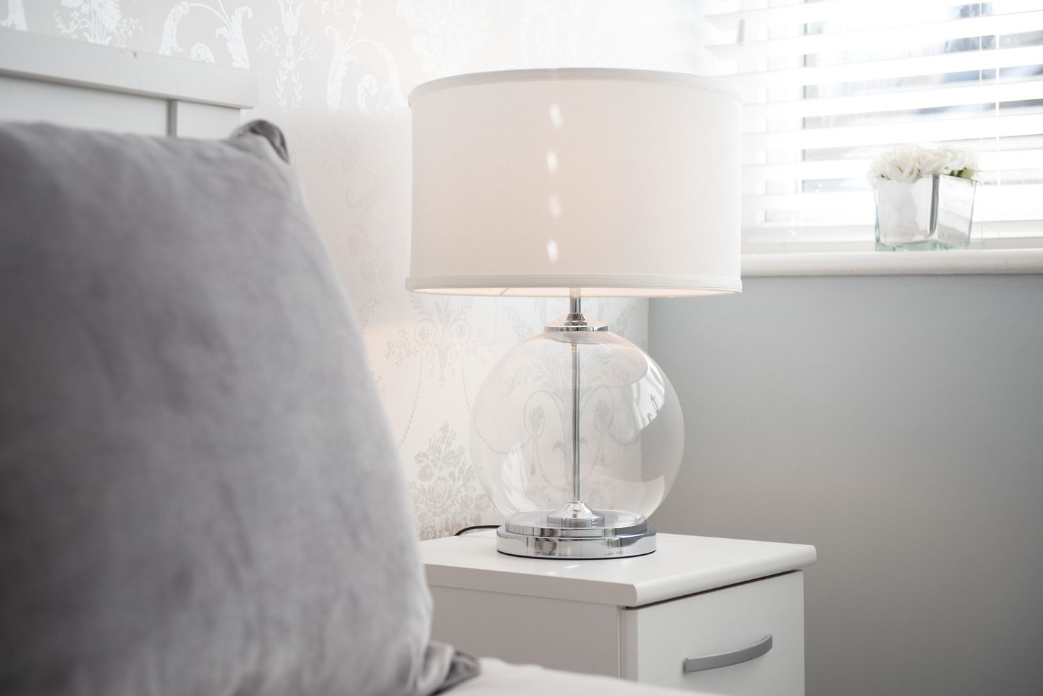 Glaslampe mit weißem Schirm auf einem Nachttisch in einem Schlafzimmer