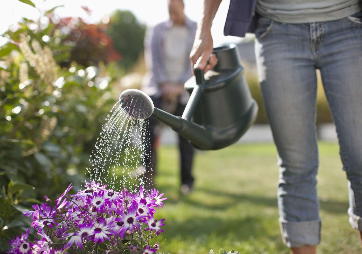 Frau gießt Blumen im Garten mit Gießkanne