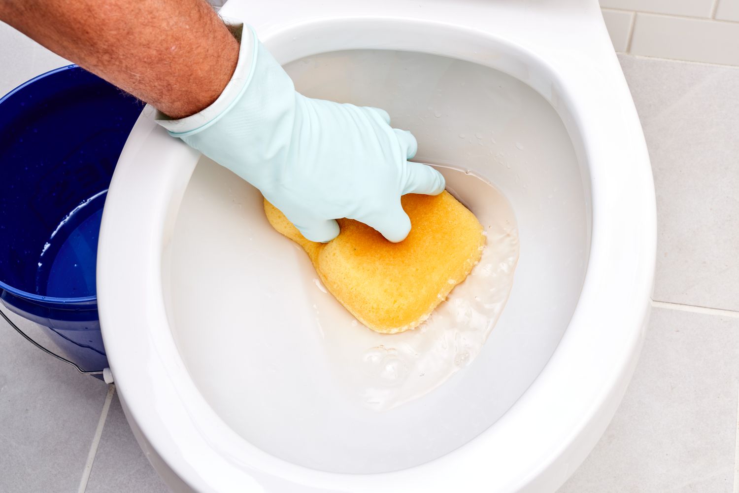 Esponja amarela absorvendo a água do vaso sanitário com luvas