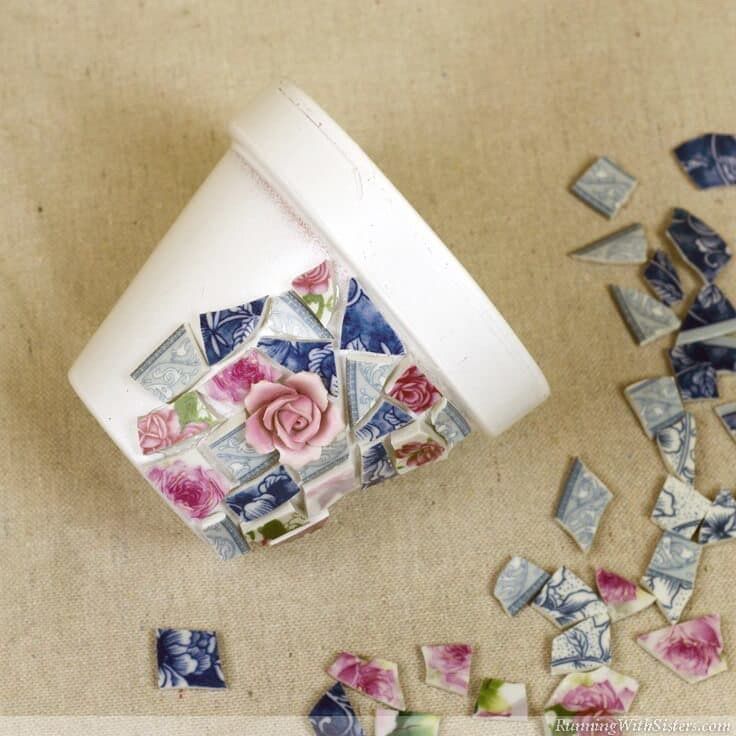 A white flower pot being covered with broken china mosaic pieces