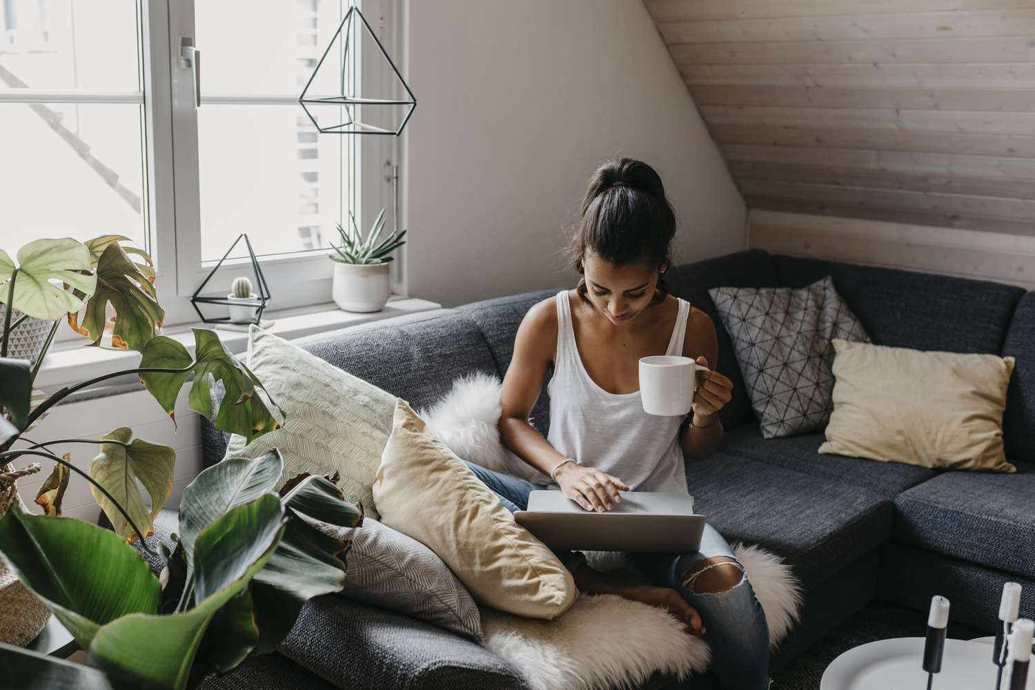 Mulher jovem sentada no sofá com uma xícara de café usando um laptop
