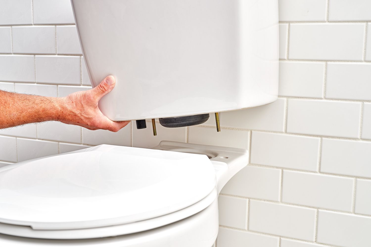 Toilet tank with bolts poking out form bottom placed on top of bowl