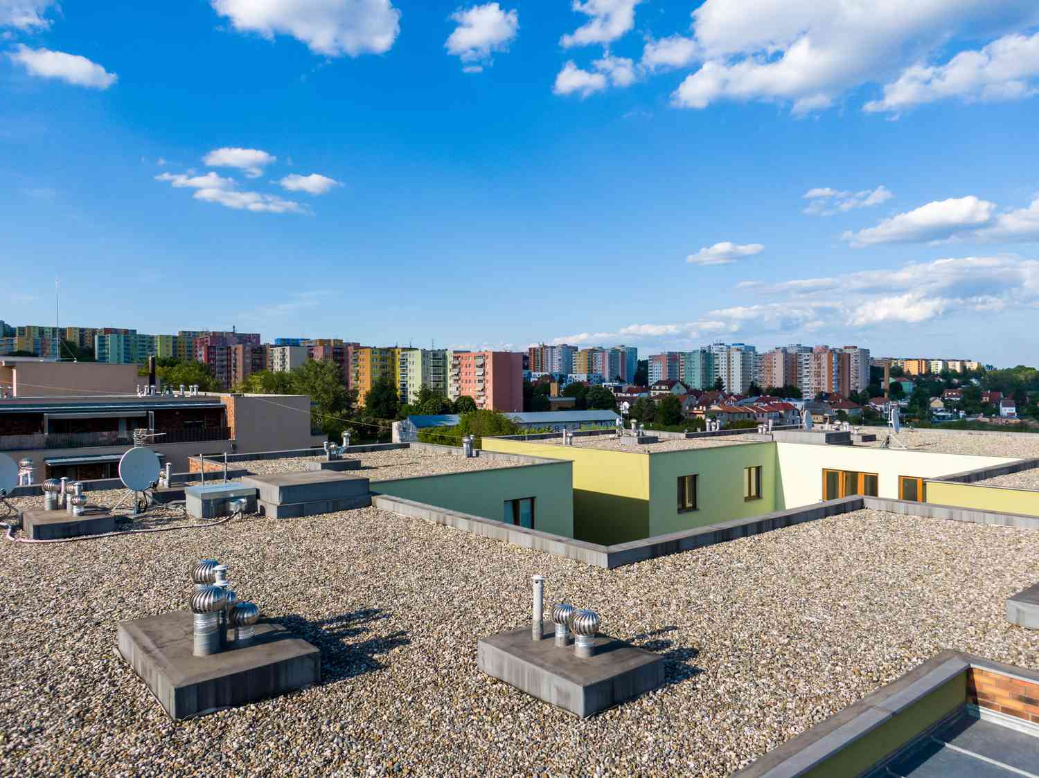 Luftaufnahme eines Flachdachs auf einem Wohngebäude. Moderne Architektur von außen. Klimaanlagen und Lüftungsstruktur. Wohngebäude im Hintergrund, sonniger Tag.