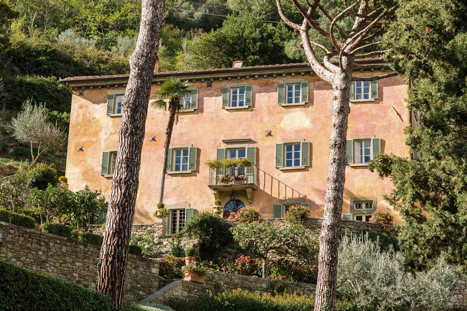 Maison de style campagne française avec des murs de couleur terre cuite entourés d'arbres et d'arbustes