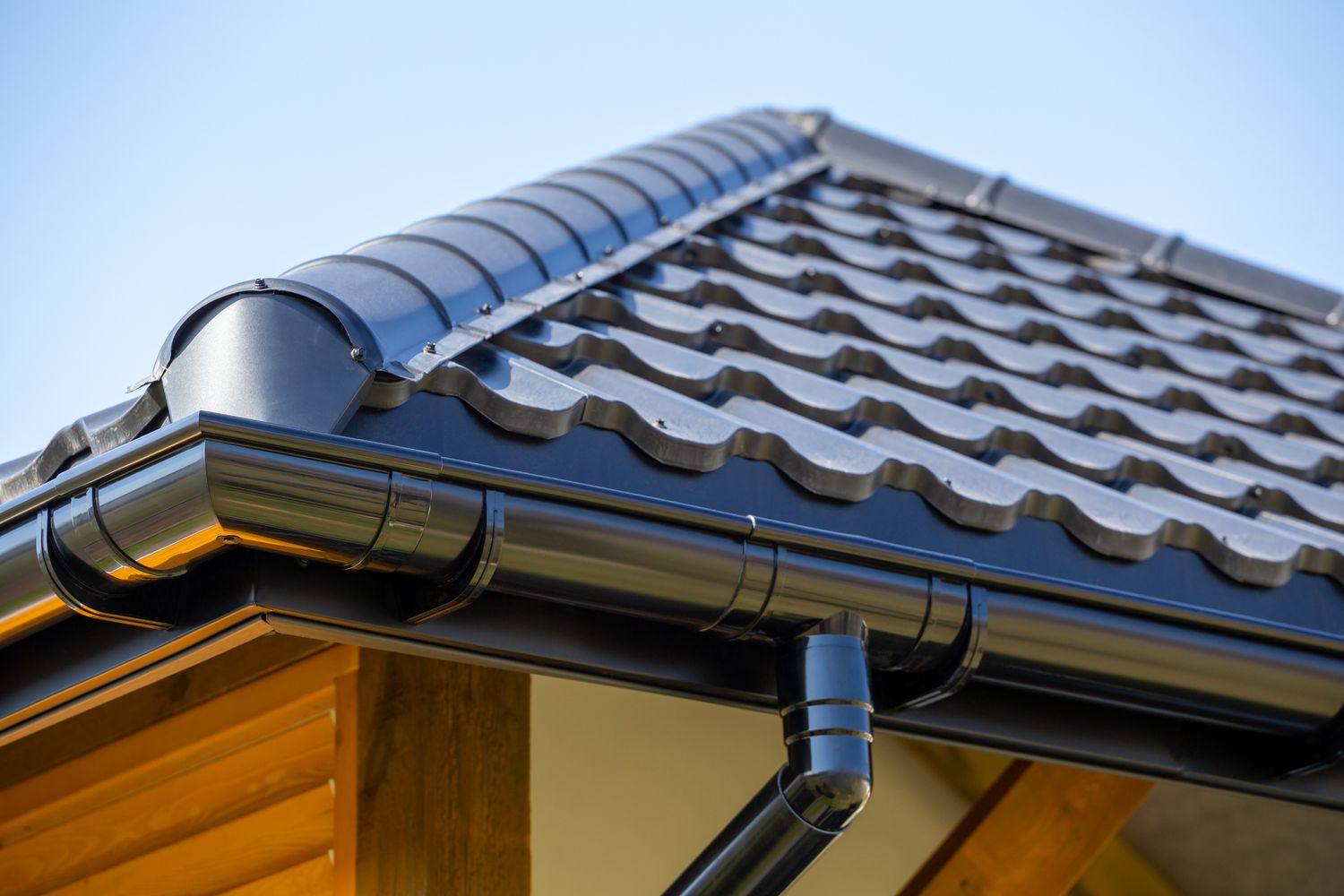 Ecke eines neuen modernen Daches mit schwarzen Dachrinnen unter blauem Himmel