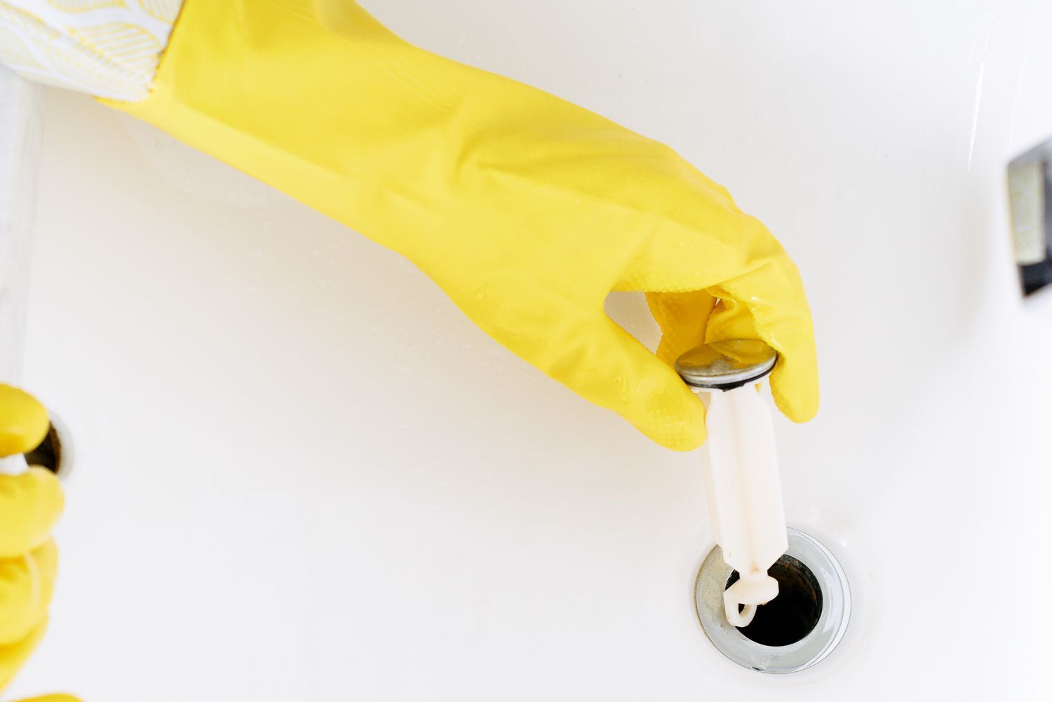Pop-up mit gelben Handschuhen aus dem Waschbecken entfernt, um den Abfluss zu reinigen