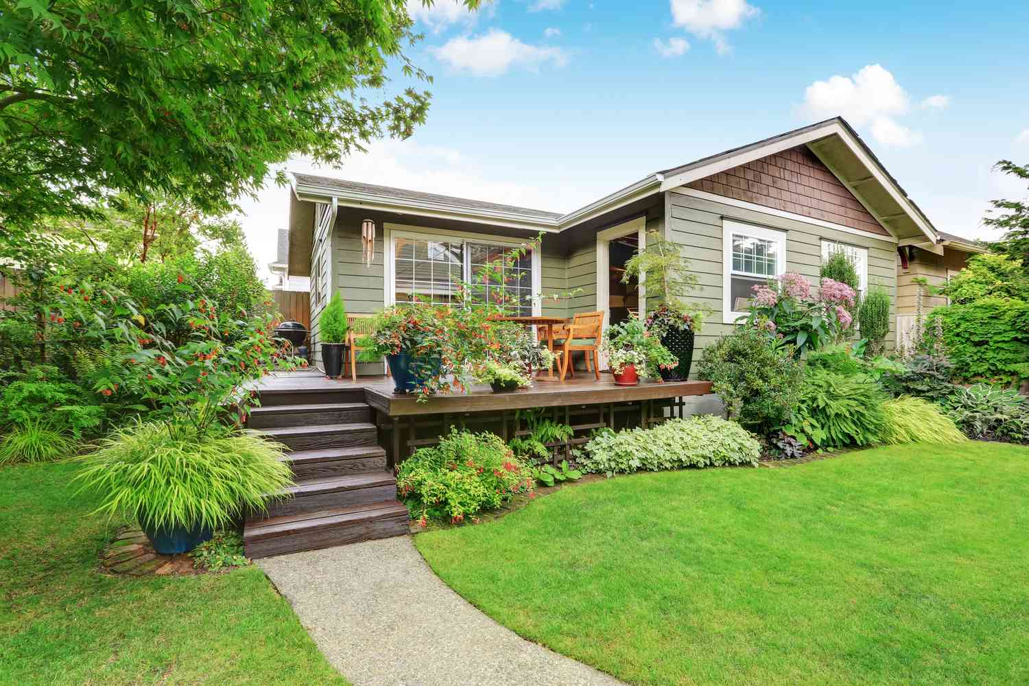 Patio trasero con jardín recortado, tarima de madera y macetas junto a casa verde