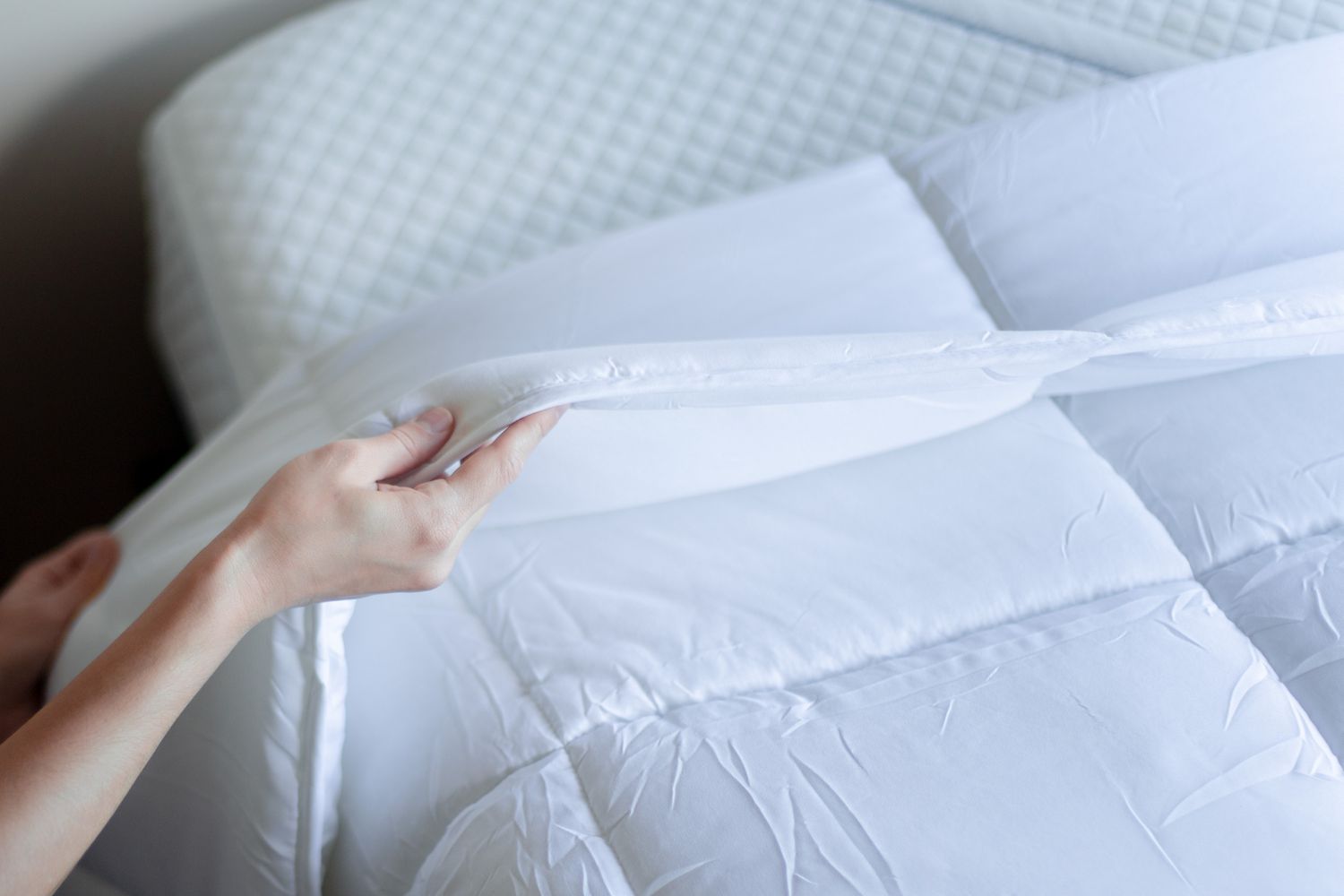 person placing a comforter on top of a mattress