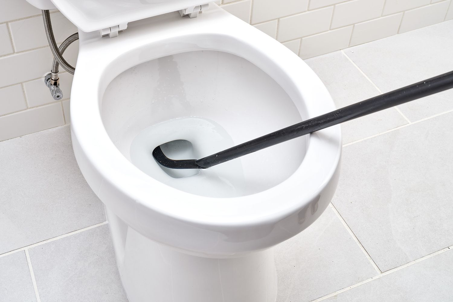 Black toilet auger inserted inside hole of toilet bowl