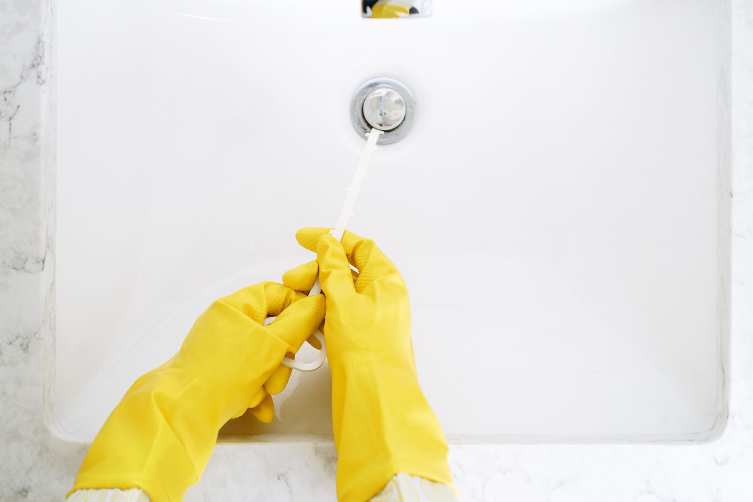 Herramienta Zip-it utilizada con guantes amarillos para limpiar el desagüe del fregadero