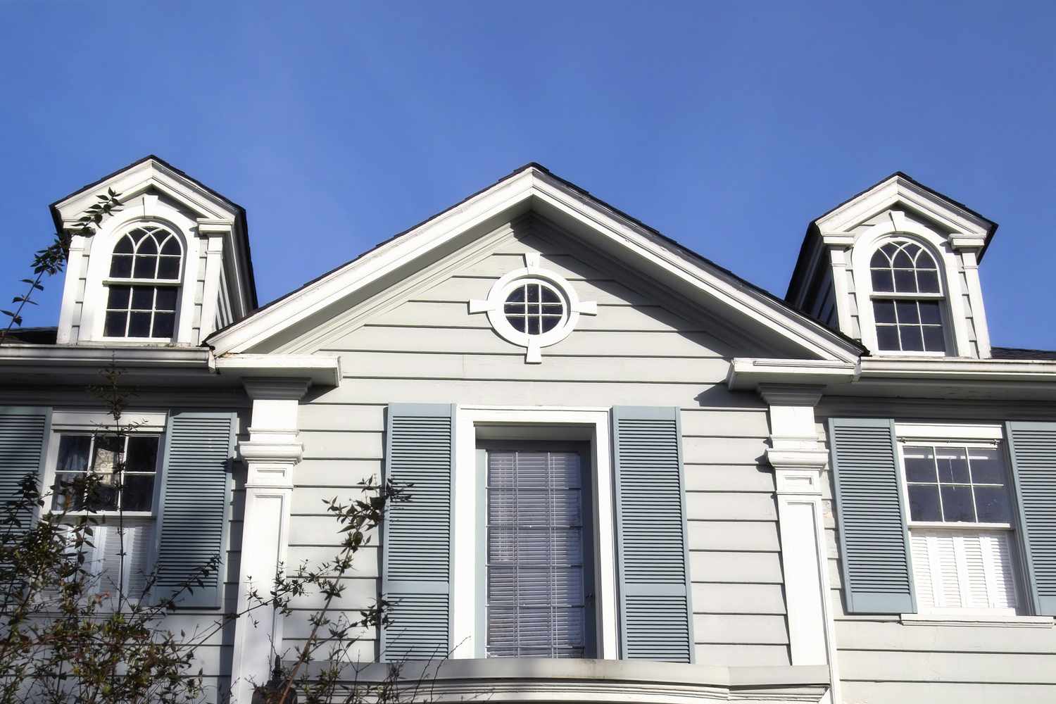 Closeup of a colonial revival home with a gabled roof and large multi-paned windows with ornate shutters