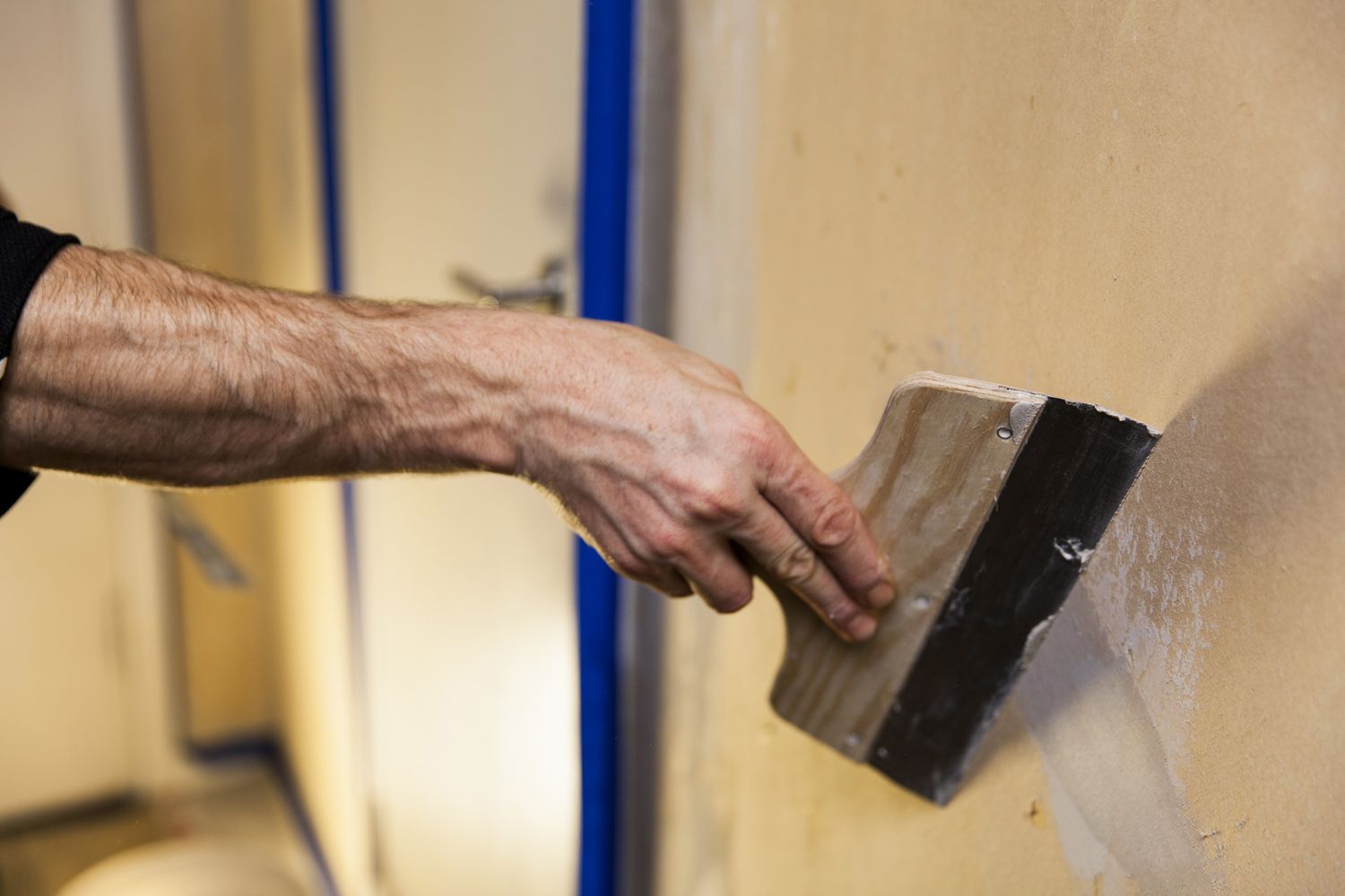 Imagen recortada de un hombre usando una escobilla de goma para rellenar un hueco en la pared