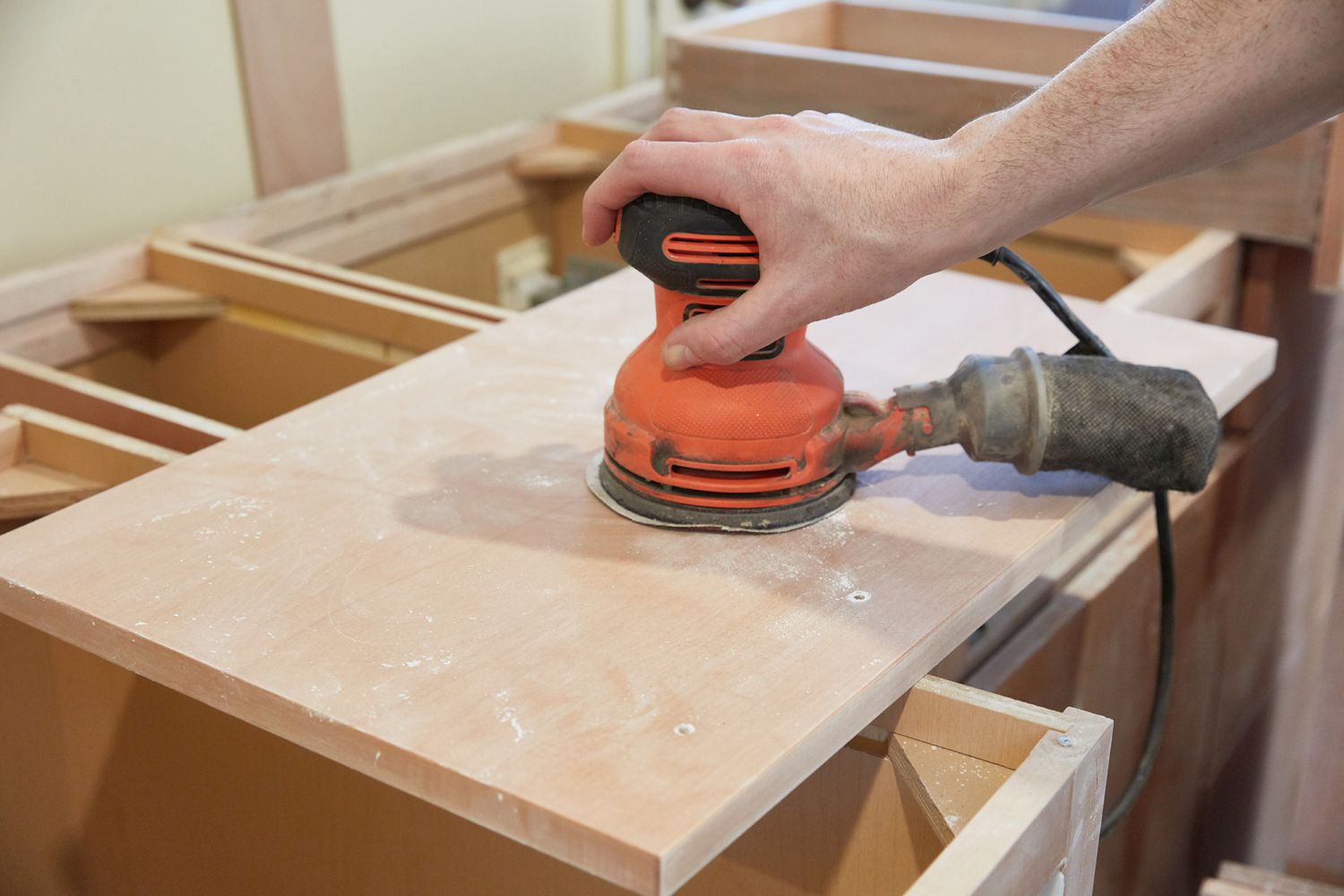 Fine-grit sander passing over kitchen cabinet surface to bring down sheen