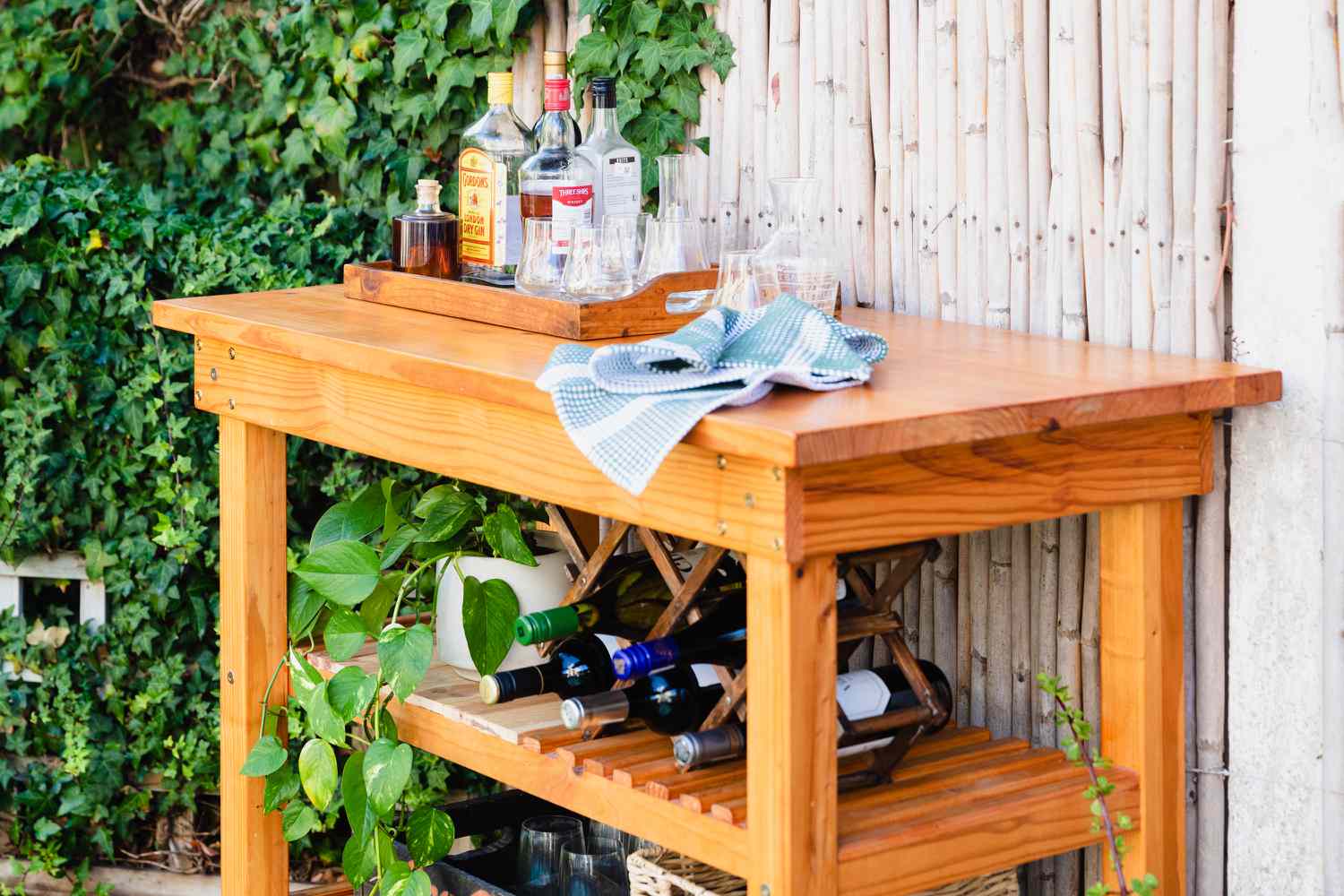 DIY-Barwagen aus Holz mit Spirituosen- und Weinflaschen in der Nähe von Pflanzen im Freien, Nahaufnahme