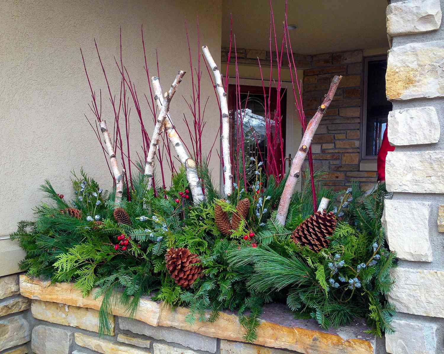 Winterlicher Blumenkasten mit Tannenzapfen, roten Zweigen, Birkenzweigen und Grünzeug