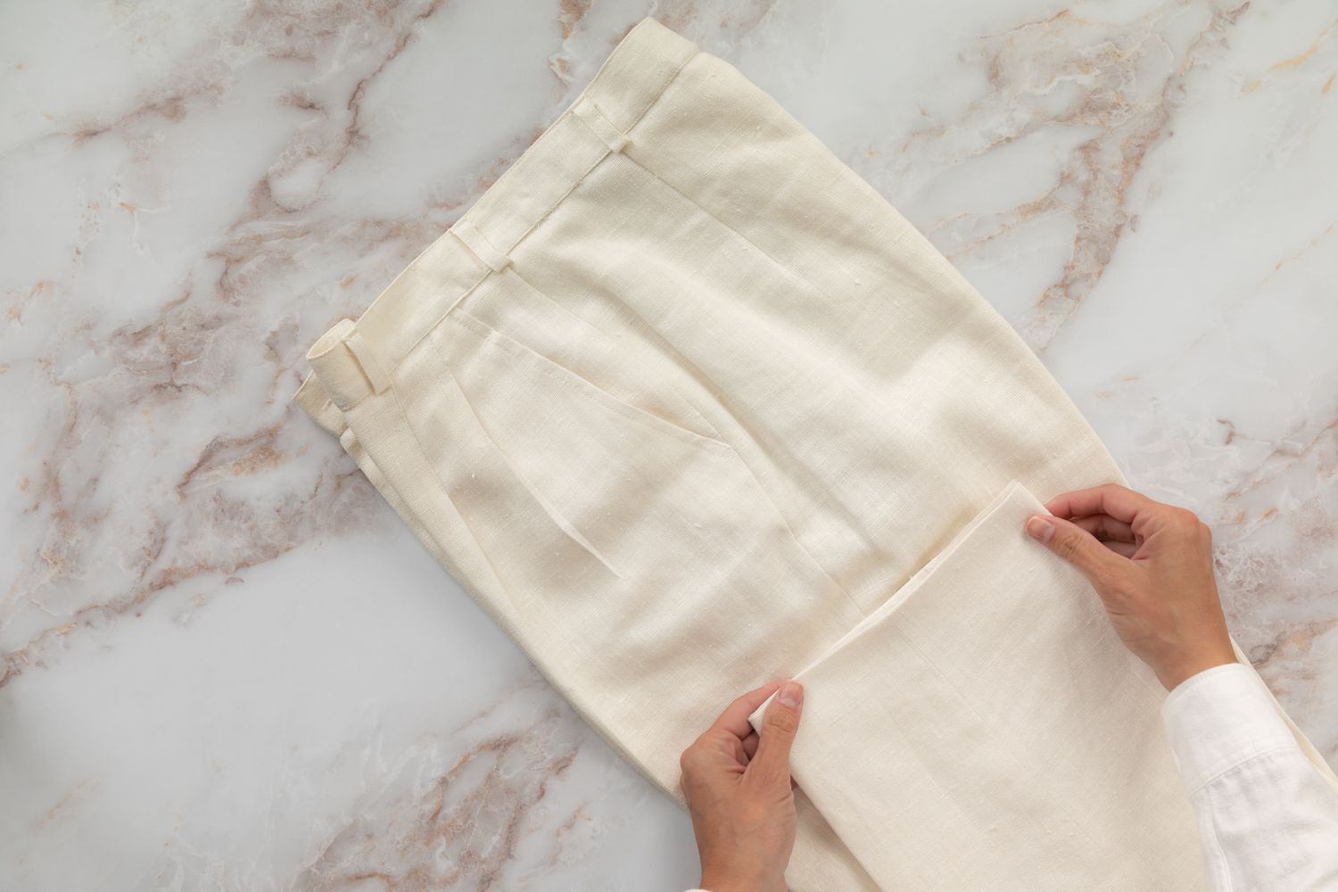 Pantalones color crema con pliegues doblados por la mitad con el puño del pantalón doblado hacia arriba hacia el pantalón de la pierna