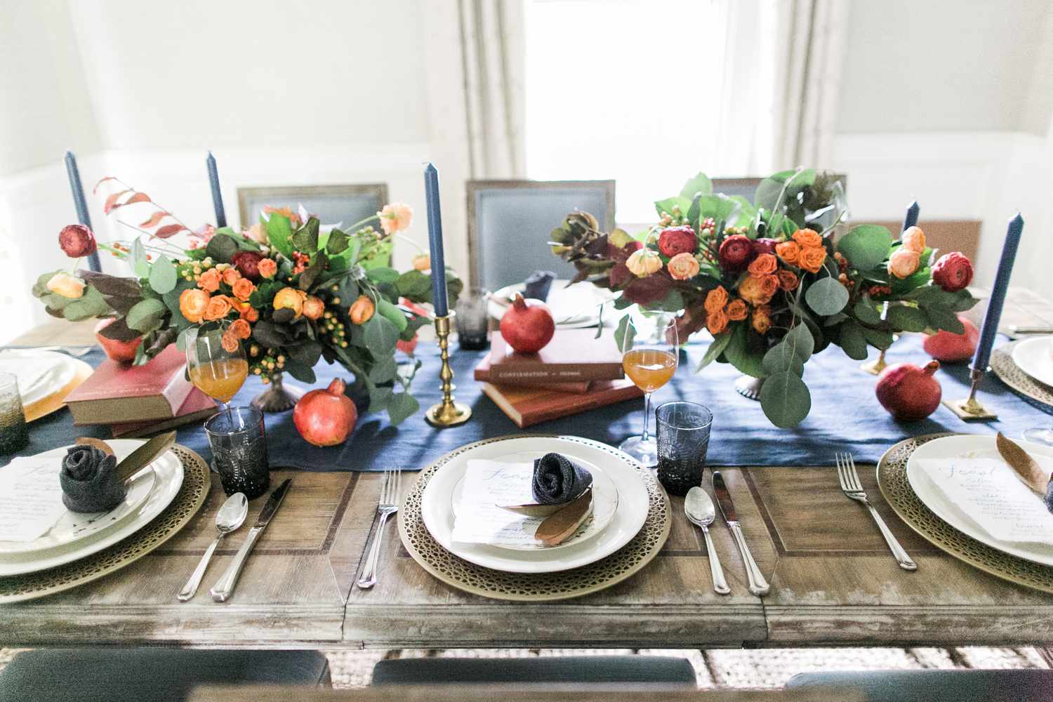 Gedeckter Holztisch mit blauem Läufer, buntem Blumenschmuck, Kerzen und weißen Tellern