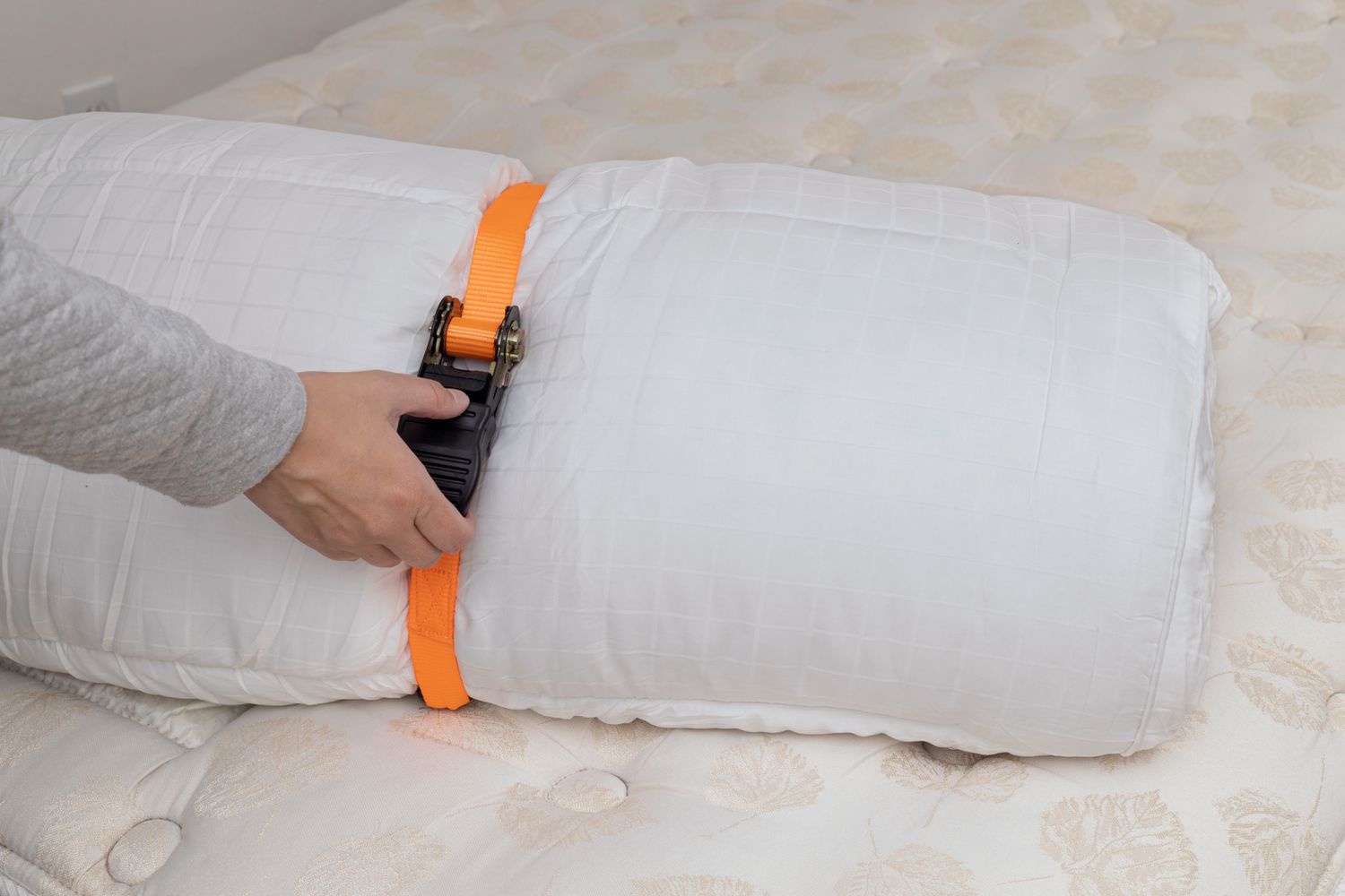 Orange ratchet strap tightened around rolled up mattress topper