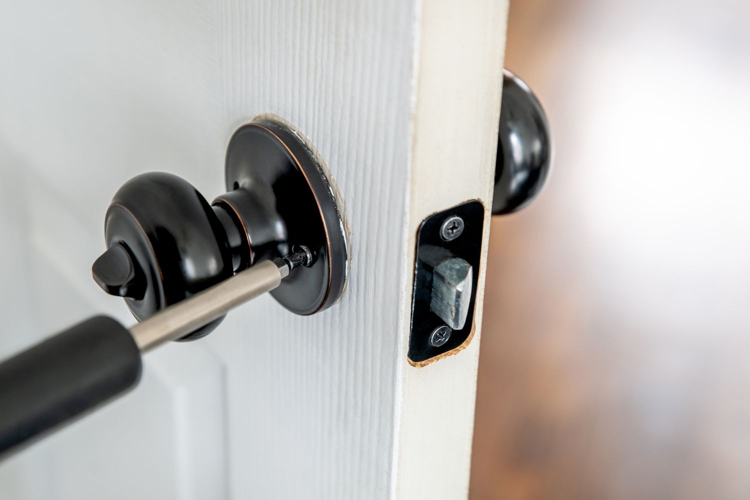 Loose door handle faceplate being tightened with screwdriver 