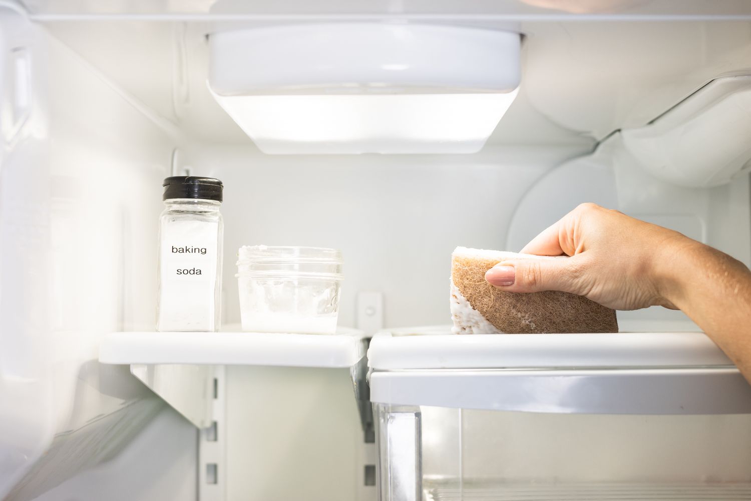 Prateleira da geladeira sendo limpa com bicarbonato de sódio, água e esponja