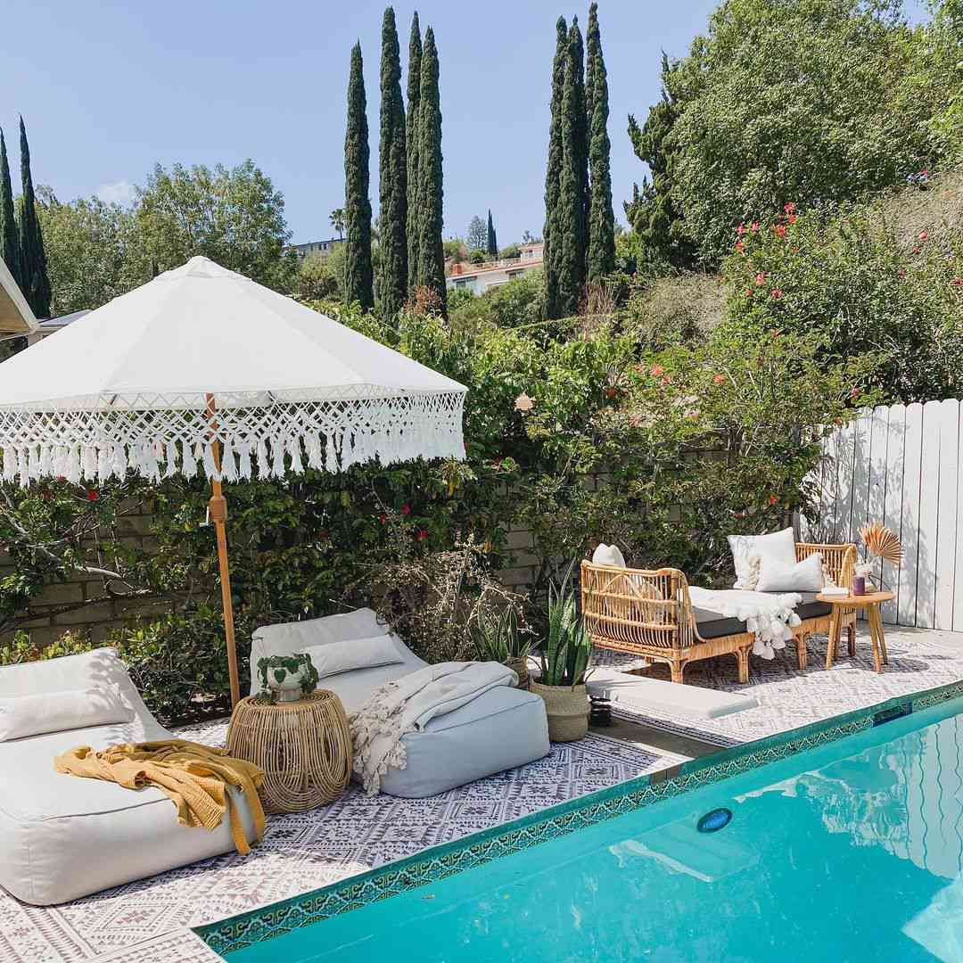 Una terraza de piscina con alfombras de exterior, tumbonas y una sombrilla de exterior