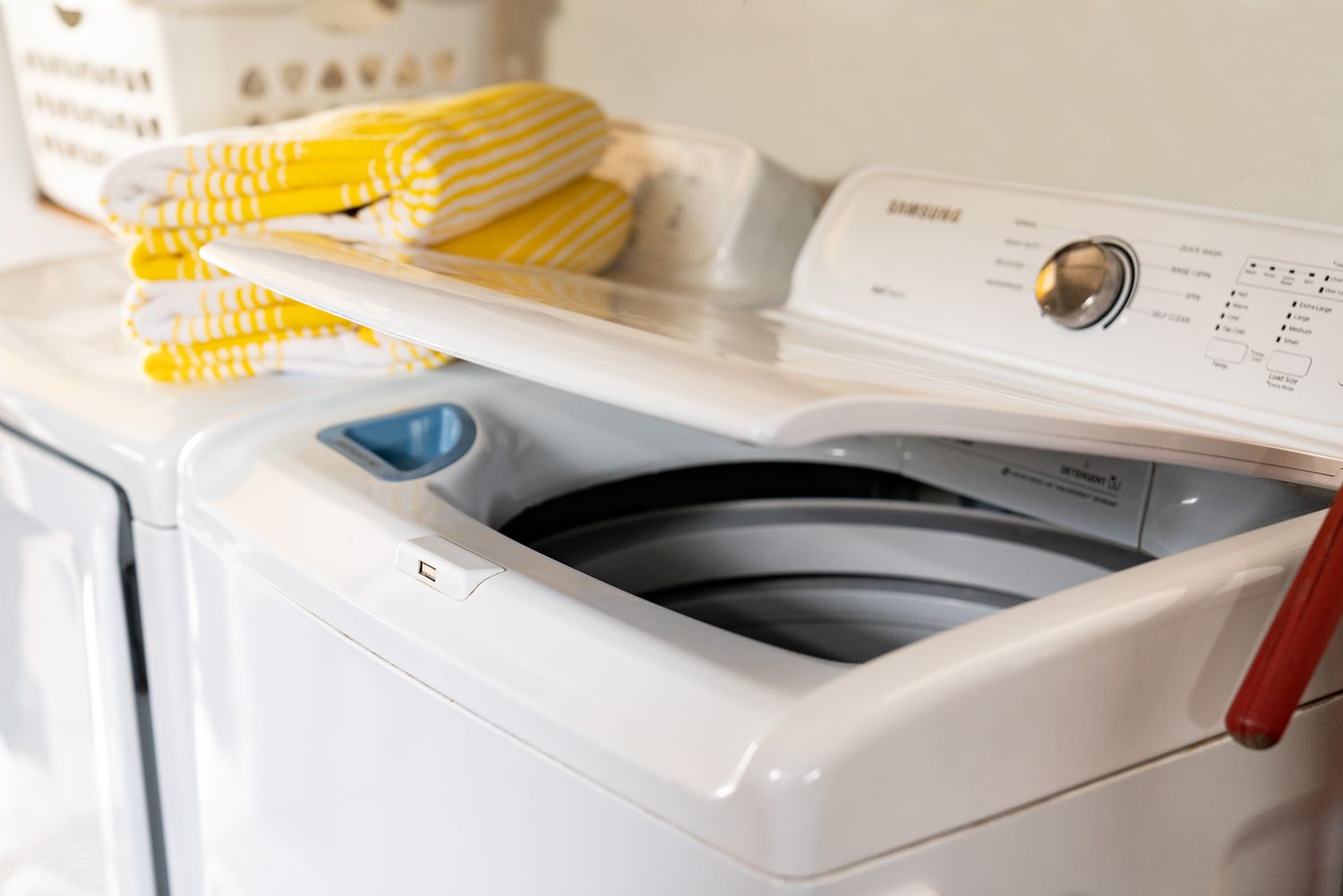 Toplader-Waschmaschine mit offenem Deckel und gefalteten gelben Handtüchern