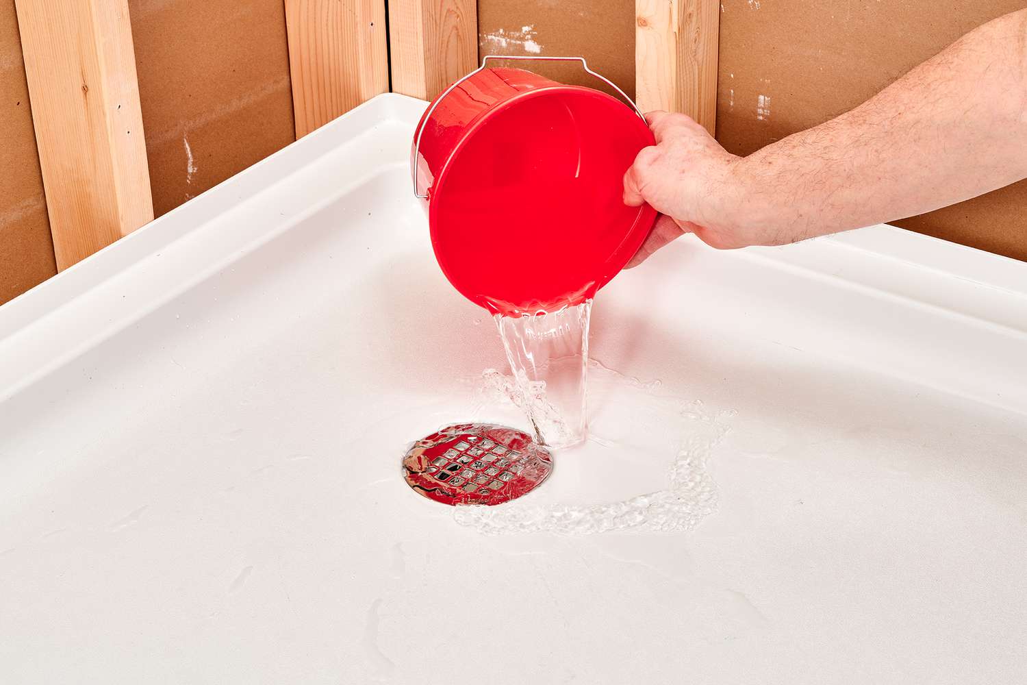 Water poured from red bucket down shower pan drain