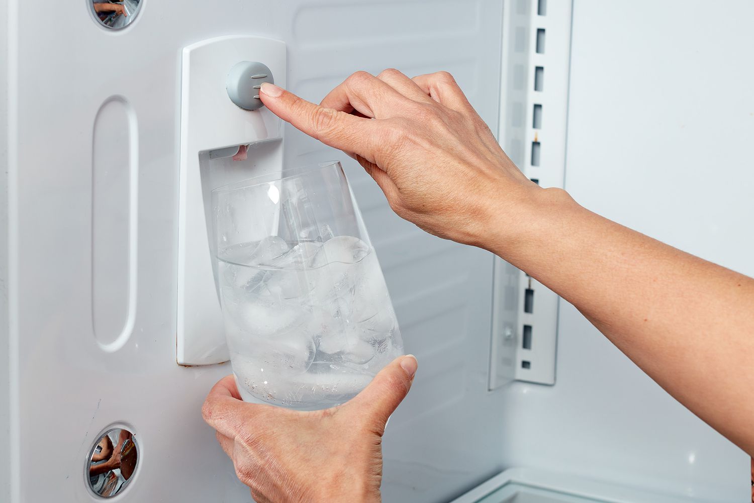 Wasser wird aus dem Kühlschrank in einen Glasbecher mit Eis gegossen