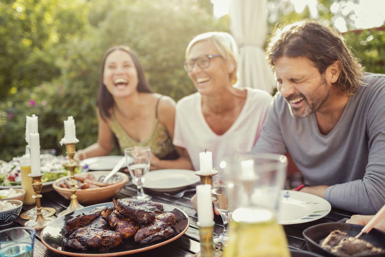 Fröhliches Paar und Freundin lachend am Esstisch während Gartenparty im Hinterhof