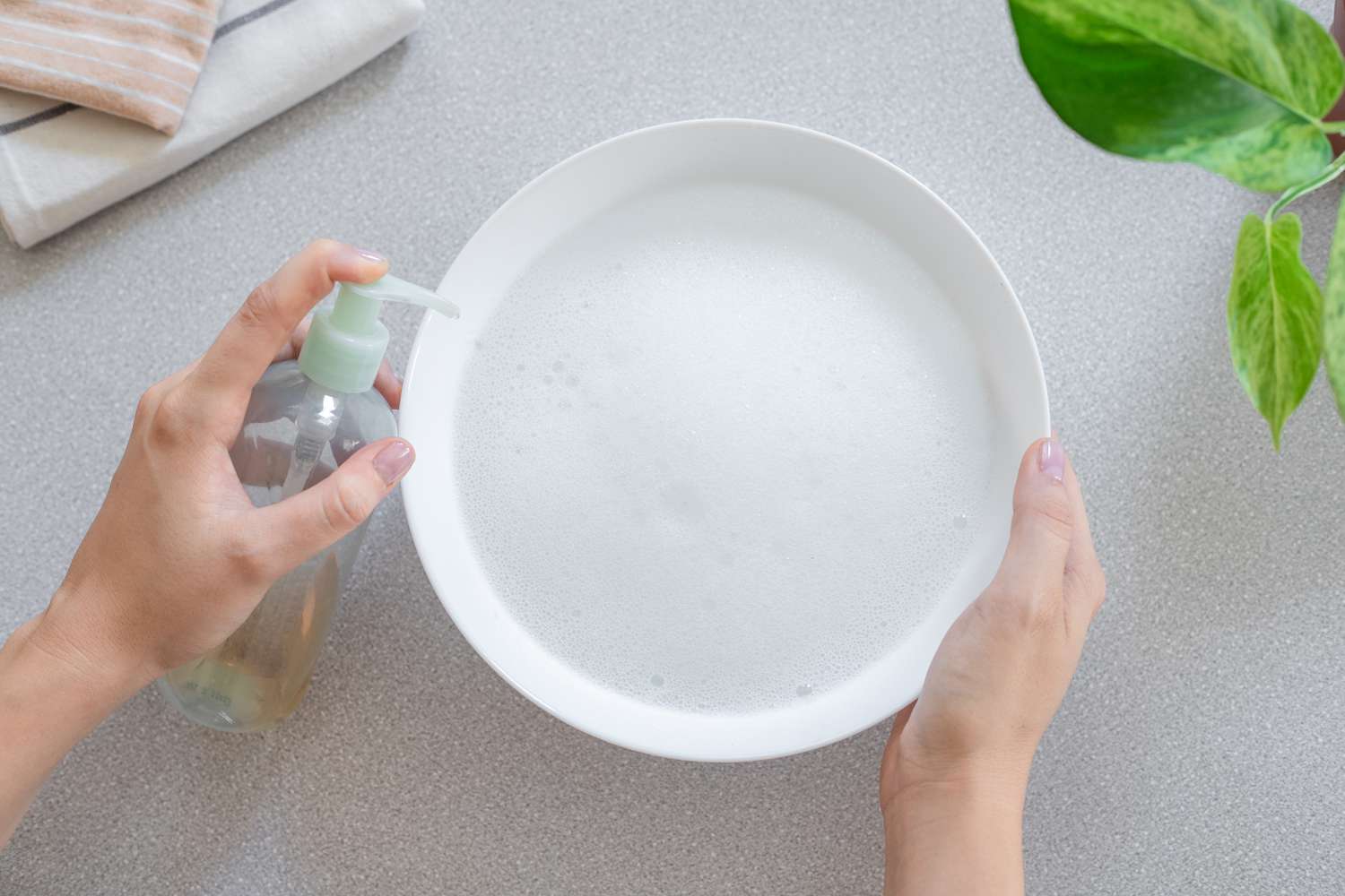 Jabón líquido lavavajillas bombeado en un cuenco blanco con agua jabonosa