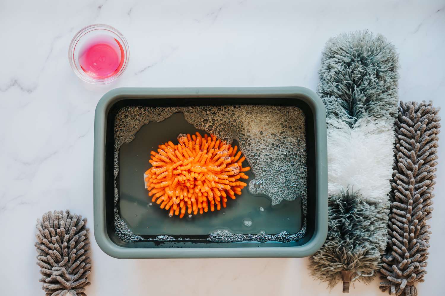 Orangenes Staubtuch in Eimer mit Wasser und Spülmittel getaucht 