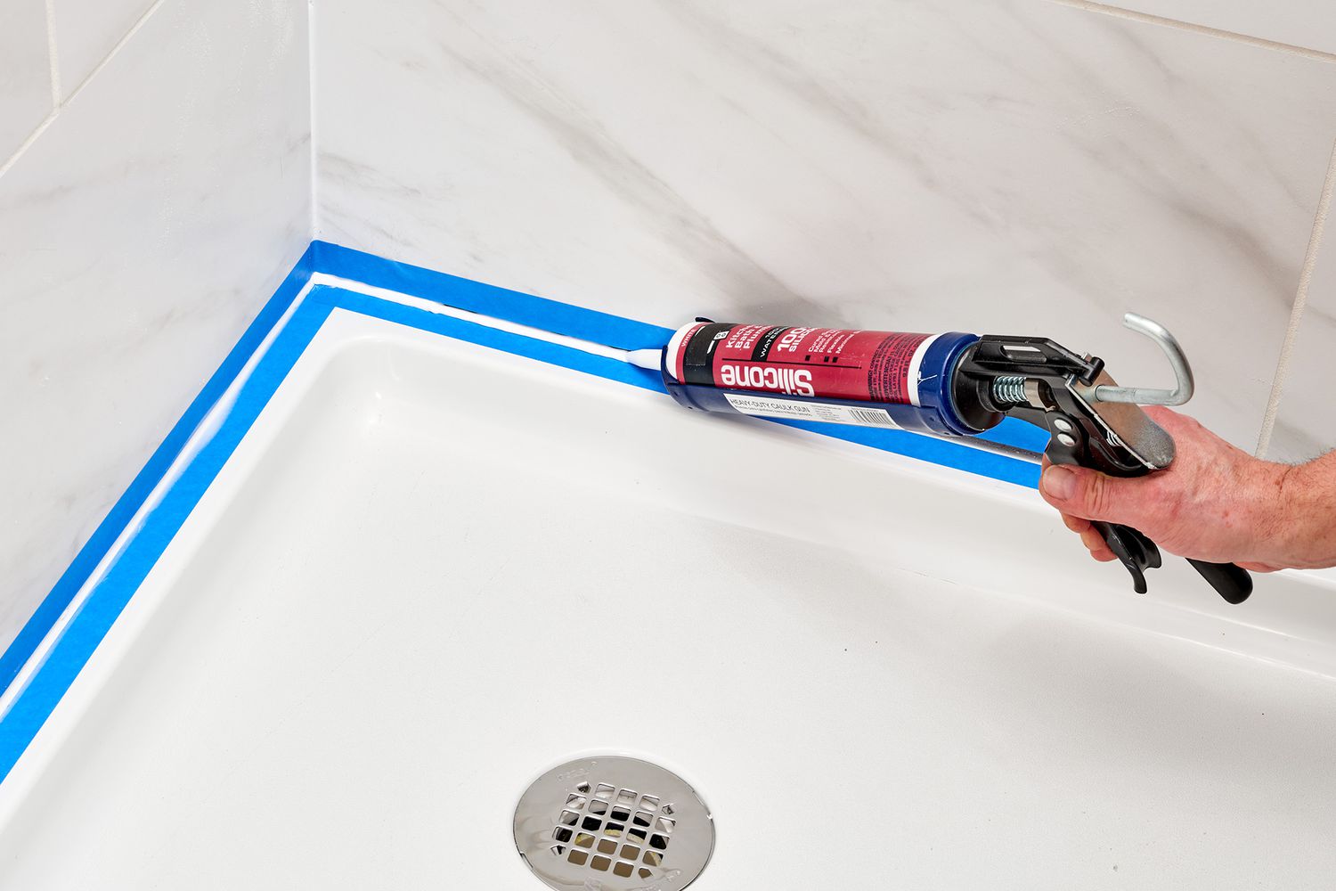 Caulk being added between shower wall and pan between painter's tape