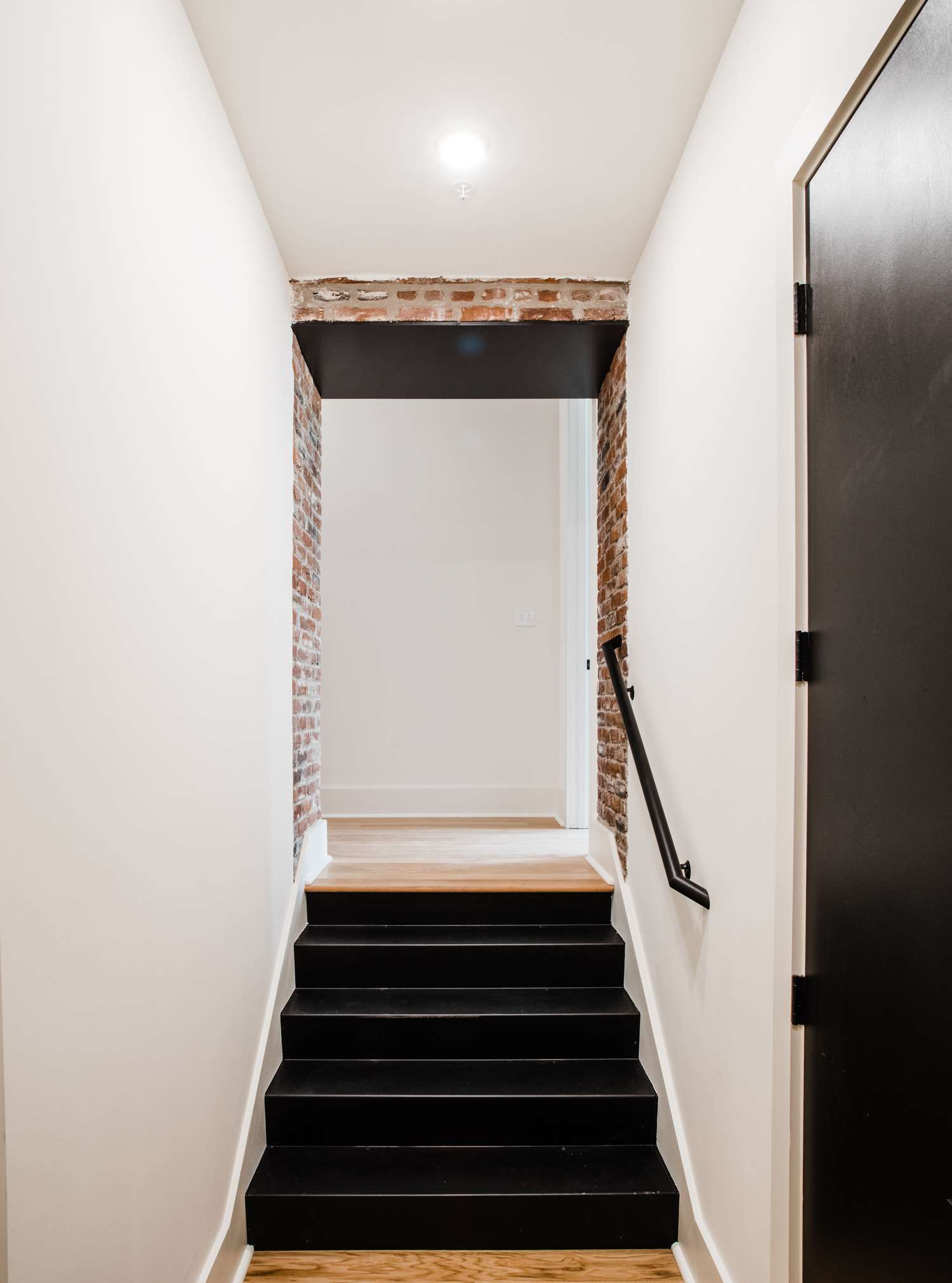 Escaleras de acero negro con ladrillo visto y paredes blancas.