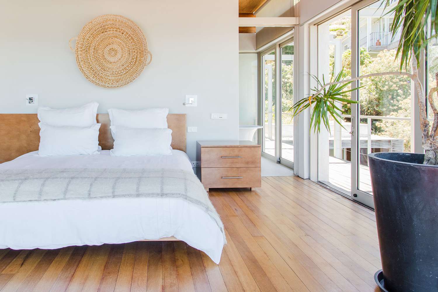 Quarto com uma cama king size, portas de vidro deslizantes, planta de palmeira e decoração circular de parede em tecido