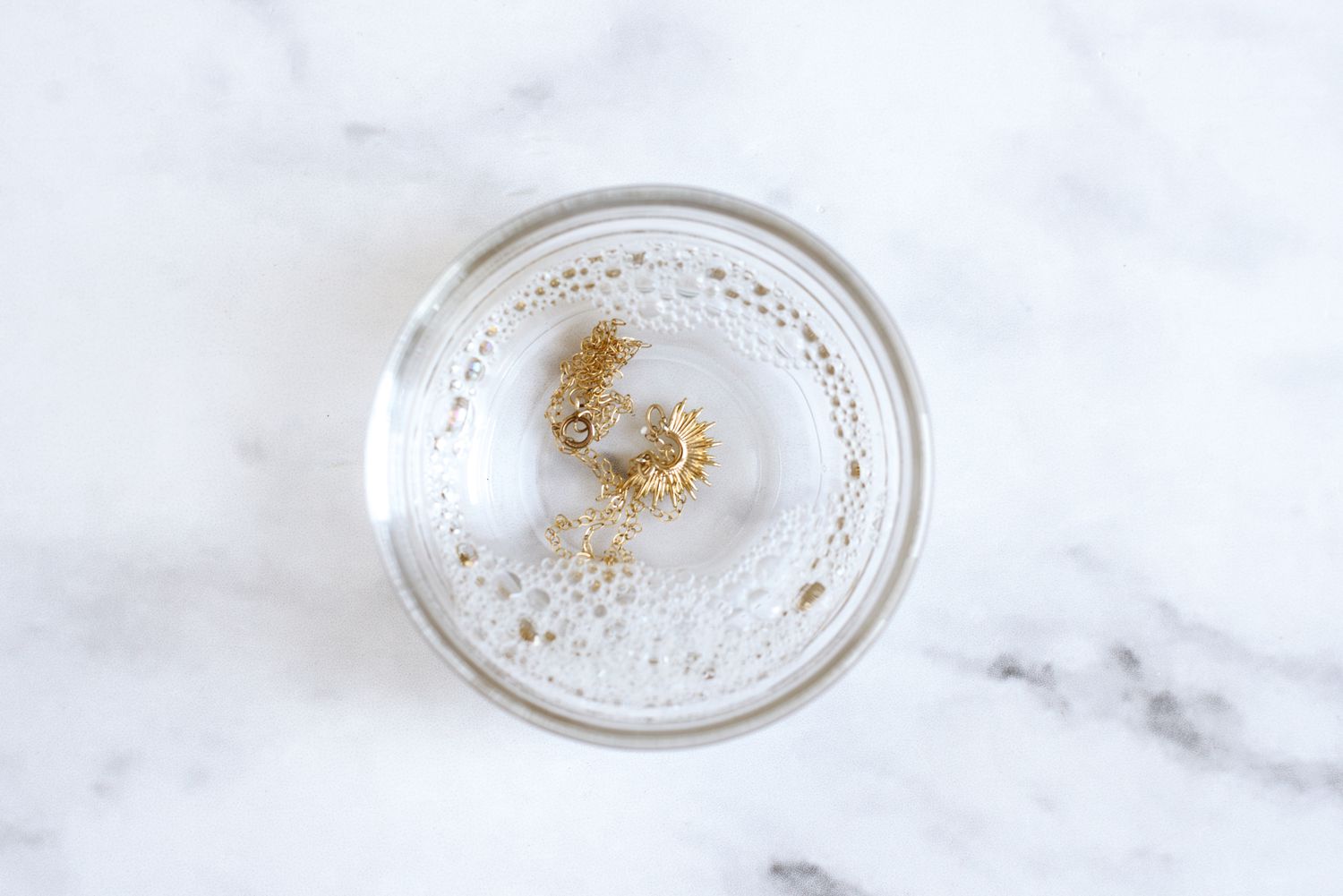 Goldschmuck in einer kleinen Glasschale mit Wasser und Spülmittel einweichen