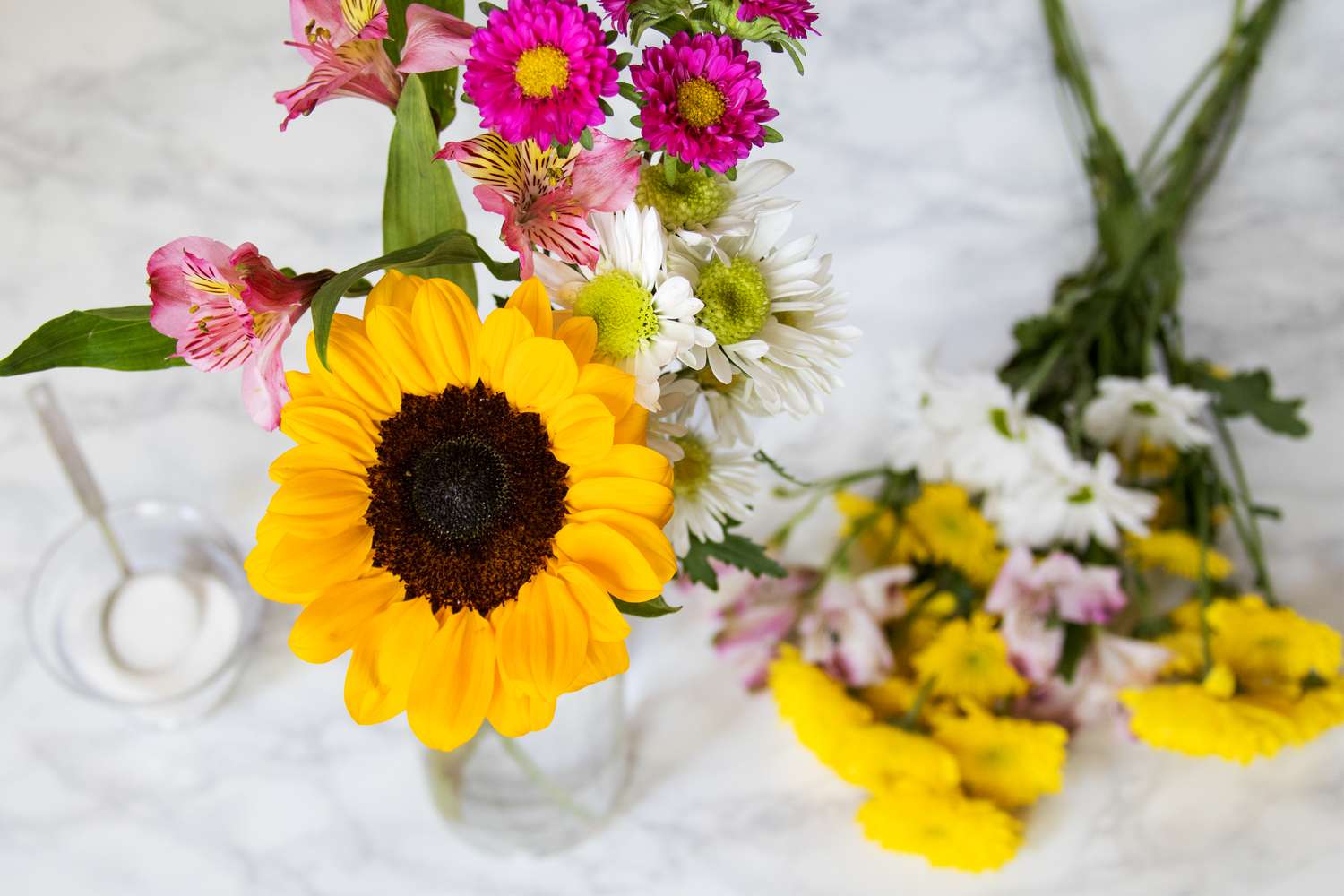 Geschnittene Sonnenblumen, Gänseblümchen und Lilien in einer Vase mit Zuckerwasser