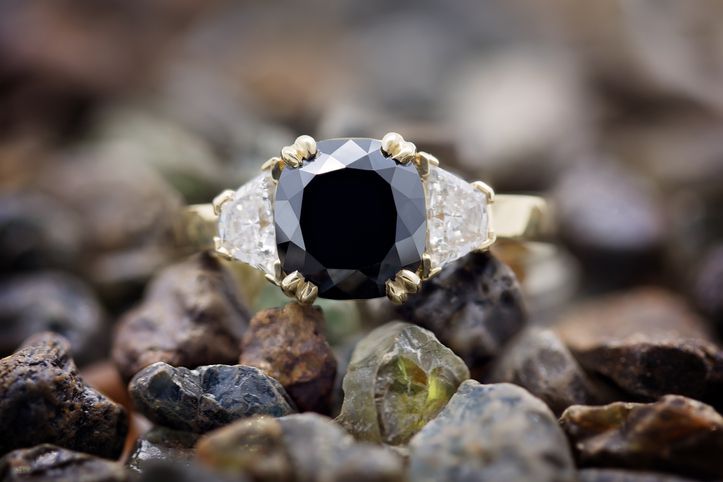 Ein großer schwarzer Diamant mit weißen Diamanten im Billionenschliff auf beiden Seiten, eingefasst in einen 18-Karat-Goldring und auf ungeschliffenen natürlichen Edelsteinen ruhend