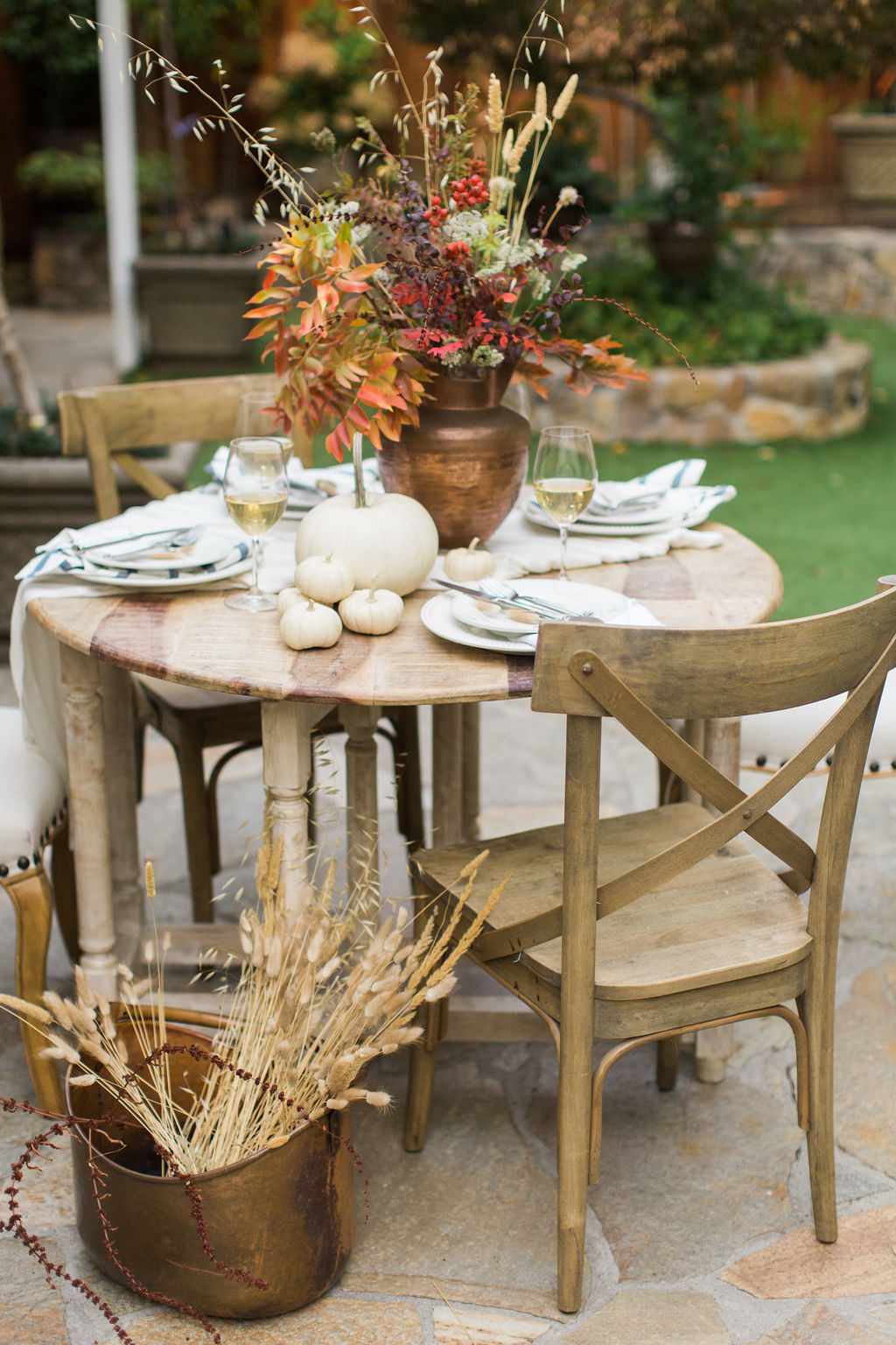 Gedeckter Tisch im Freien mit großem Blumenschmuck und weißen Kürbissen