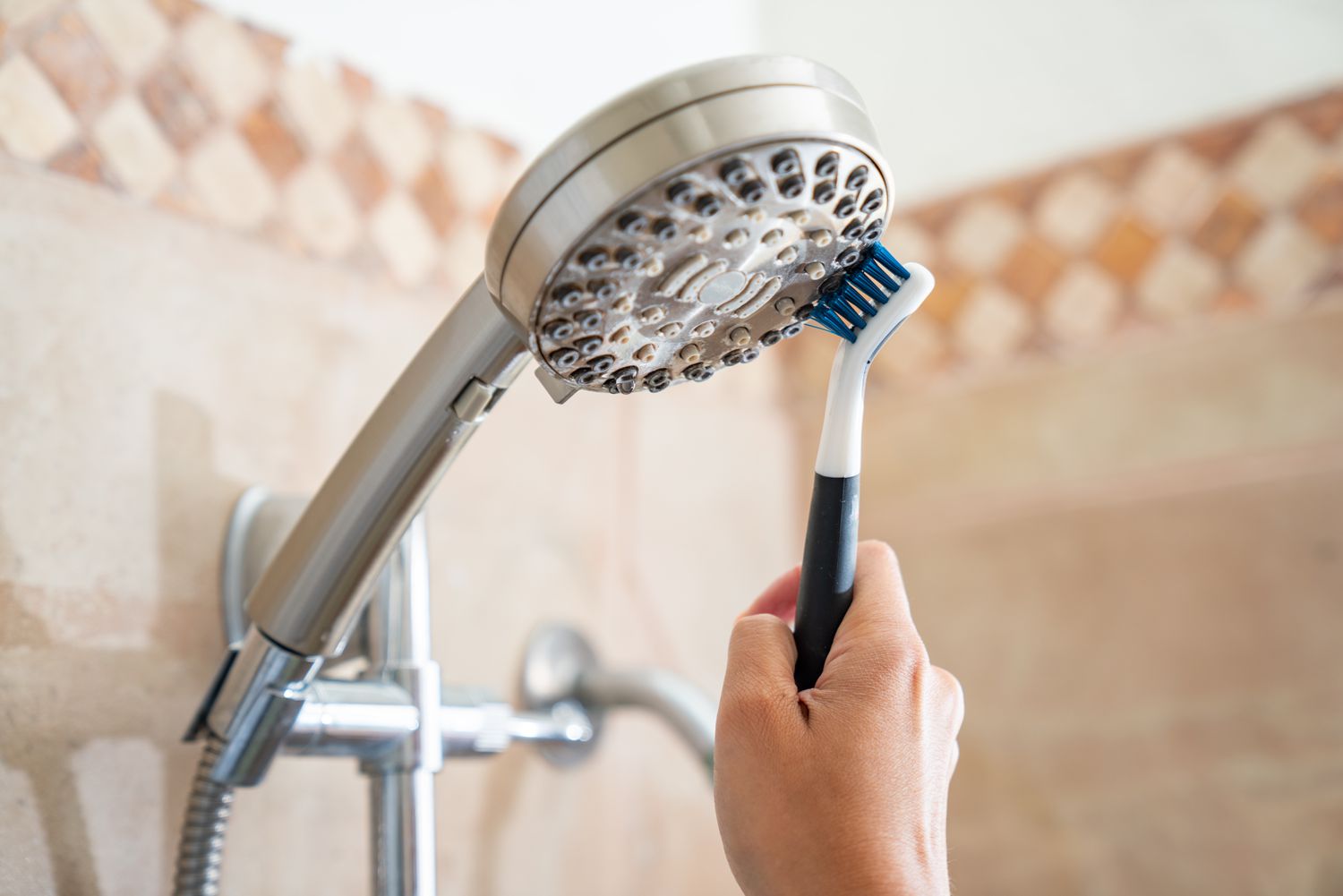 Shower head being scrubbed with old toothbrush to remove soap scrum