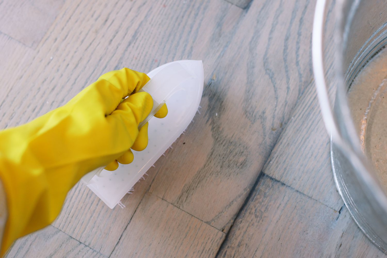 Escova dura esfregando o piso de madeira com detergente neutro e desinfetante