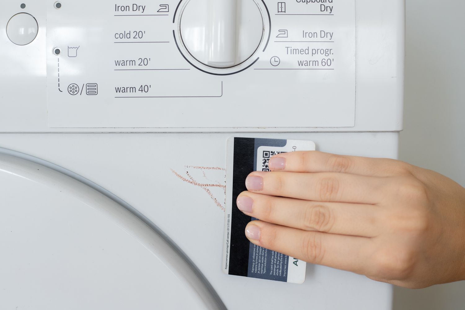 Credit card edge scraping off melted wax from exterior of washing machine