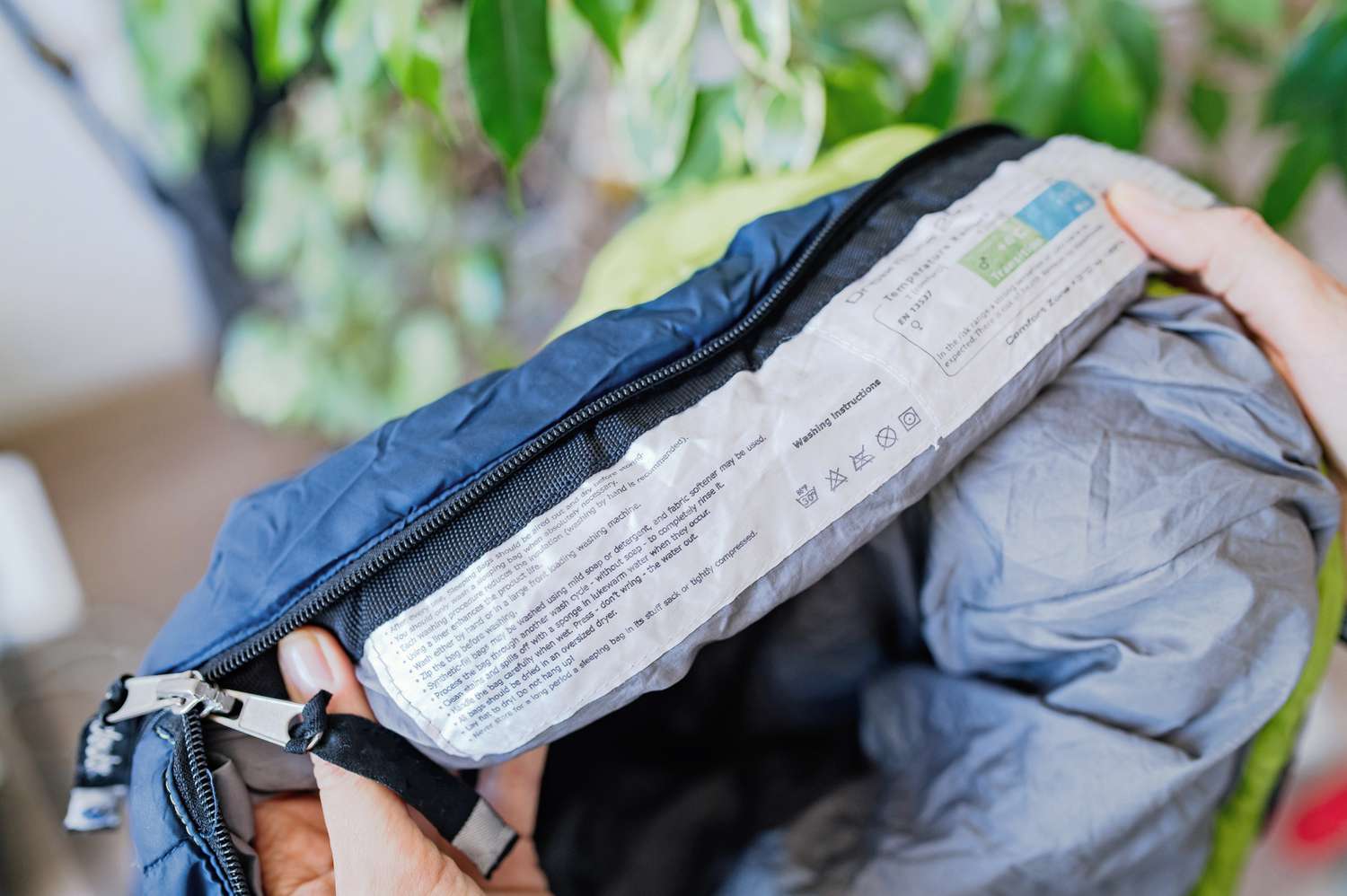 Pflegeetikett vom Kunstfaserschlafsack vor der Reinigung hochgehalten