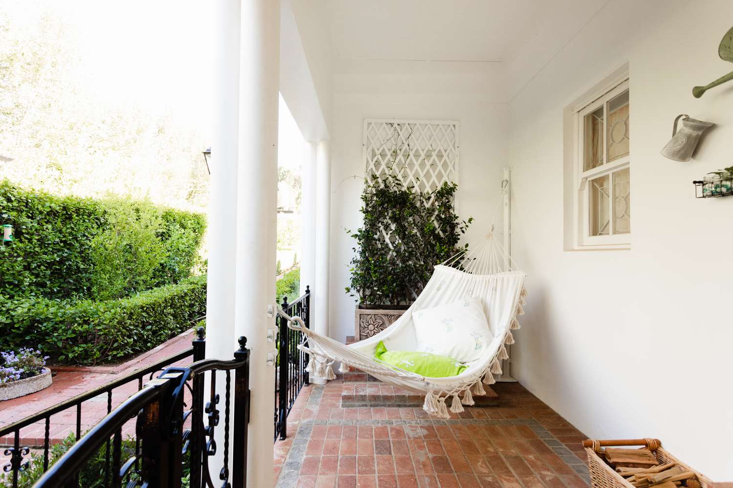 Veranda im Freien mit Backsteinboden und weißer Hängematte zwischen Wand und Säule