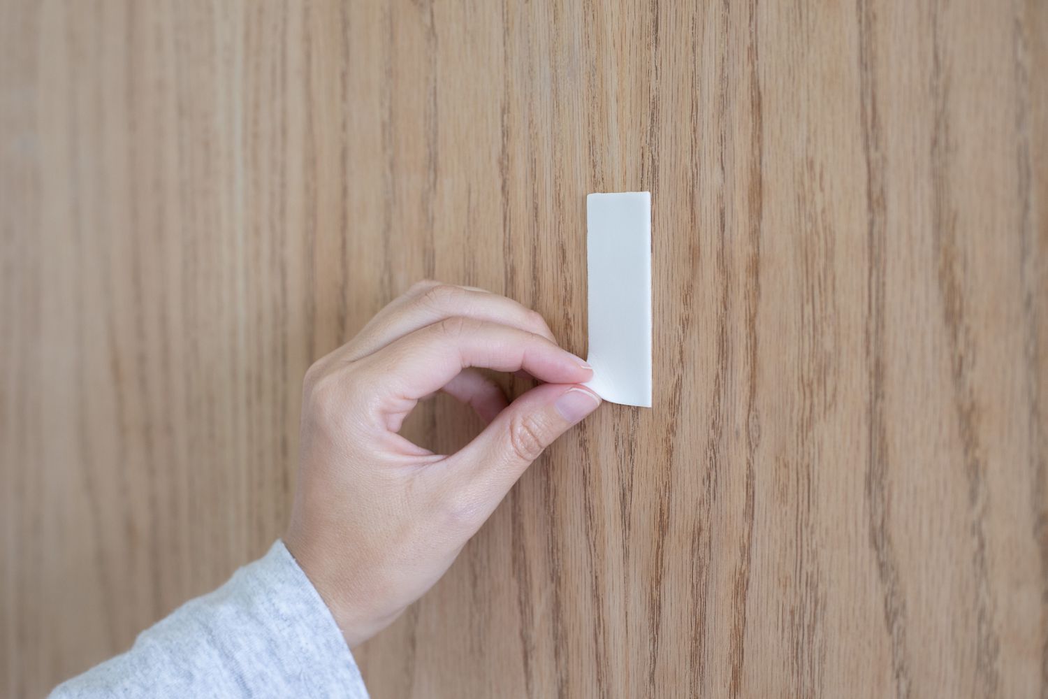 Double-sided tape on wood wall being peeled off by hand