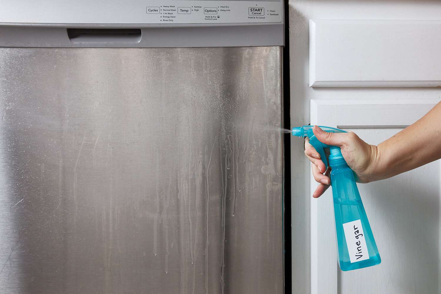 person using vinegar spray on stainless steel