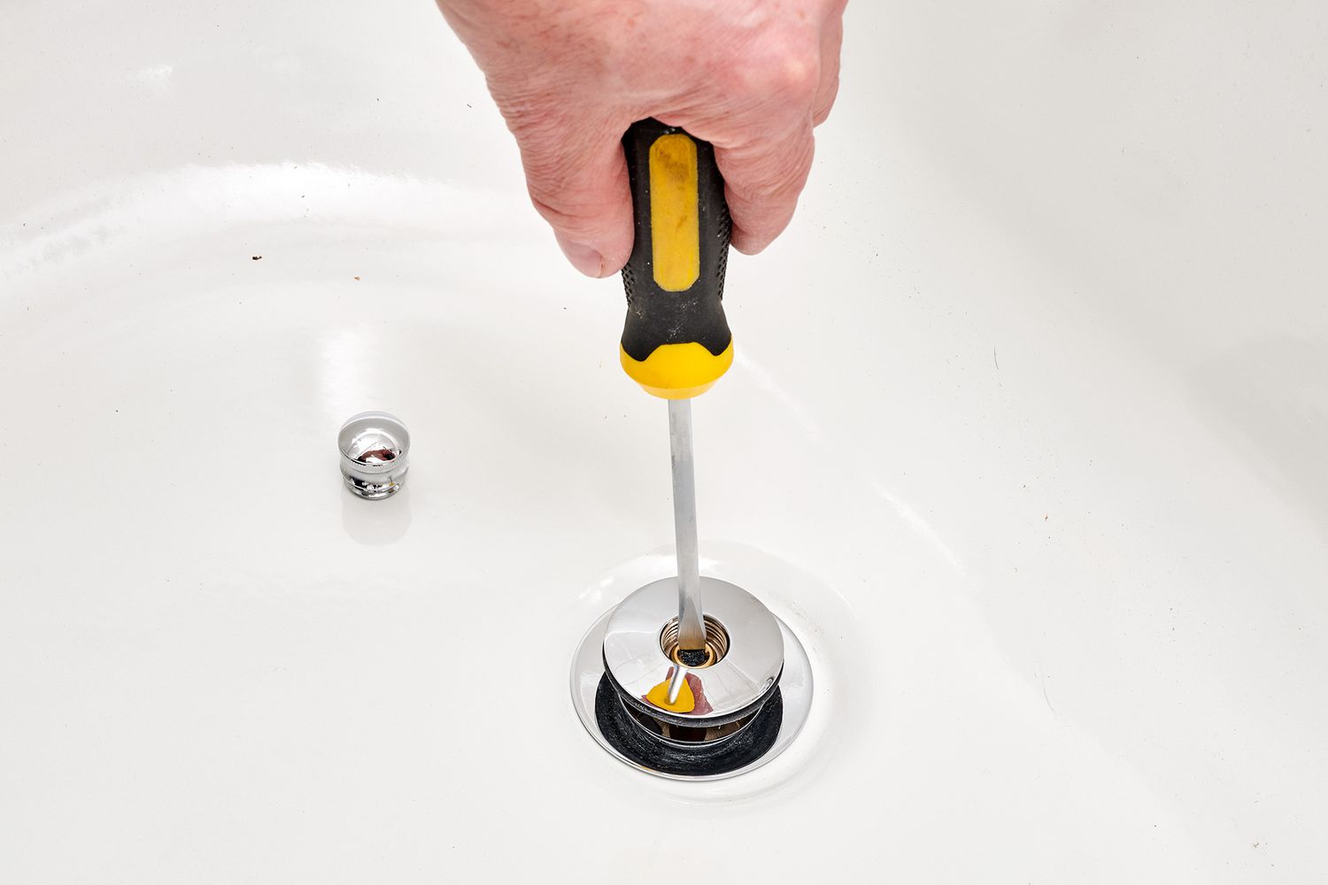Screwdriver removing lift-and-turn drain stopper bolt from drain hole