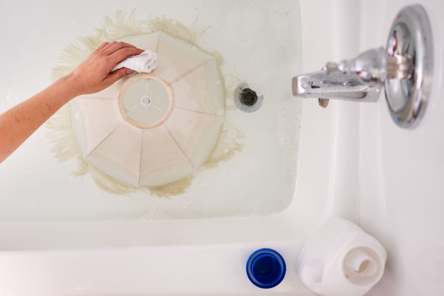 Abajur branco de molho na banheira com solução de limpeza e esfregado com pano de microfibra branco