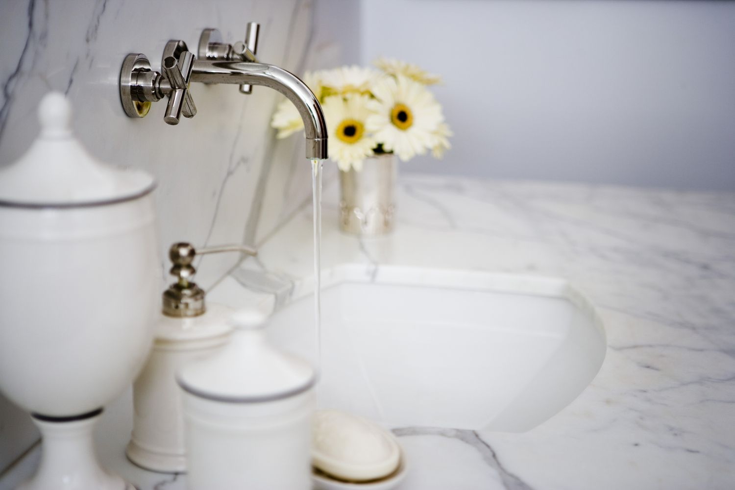 Lavabo del tocador con grifo abierto, jarrón de flores y accesorios de baño