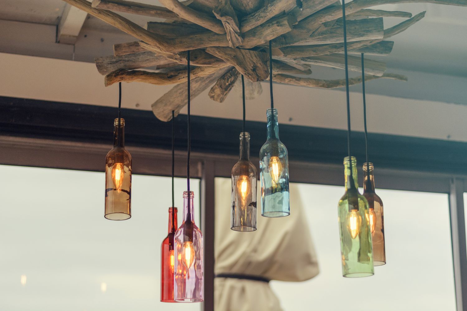 colorful bottles with lightbulbs in them turned into pendant lights hanging from drift wood on the ceiling